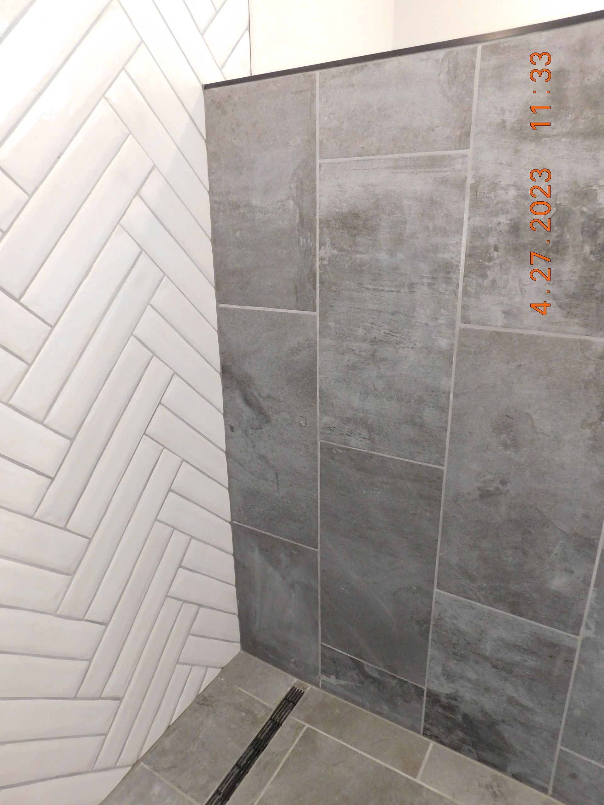 Modern bathroom shower corner with white herringbone tile and gray stone tile wall.