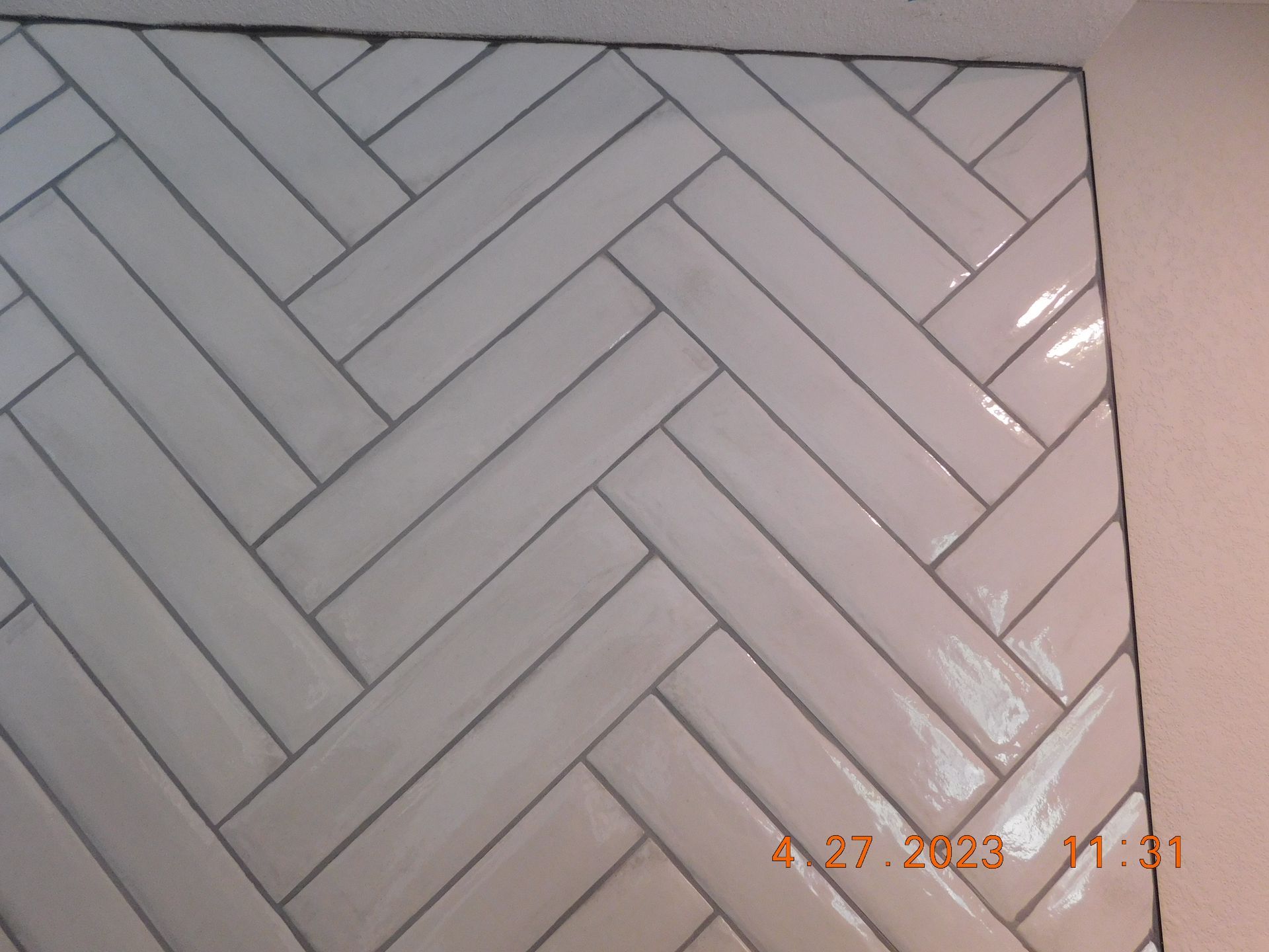 White herringbone tile wall with dark grout and a small orange date stamp in the bottom right.