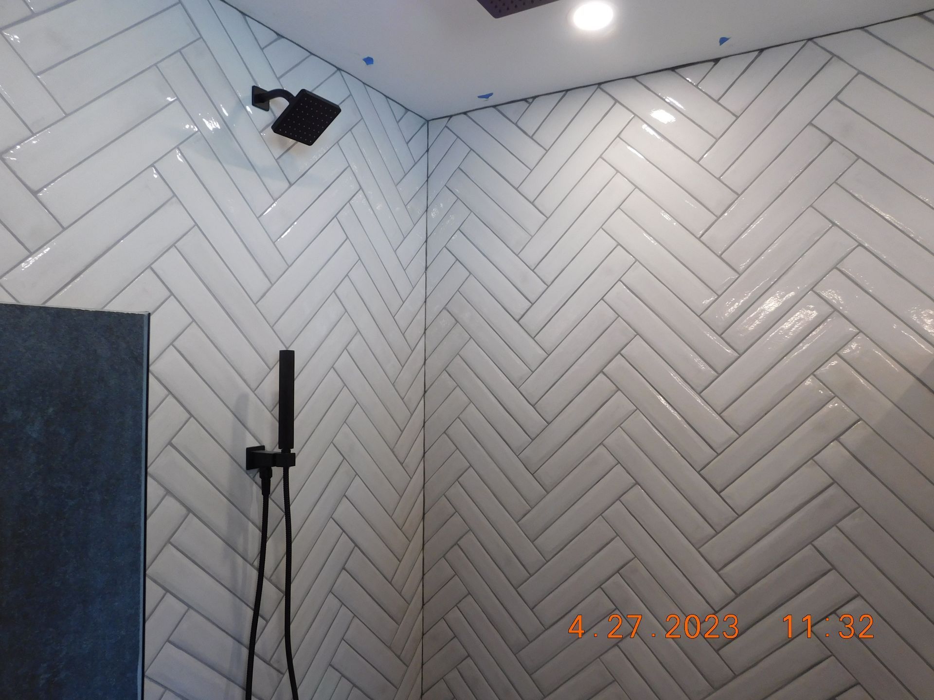 White herringbone tiled bathroom wall with shower fixtures and recessed ceiling lights