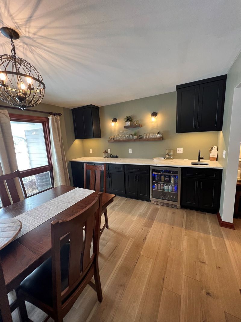 Modern kitchen with dark cabinets, wood floors, and a wooden dining table by a window