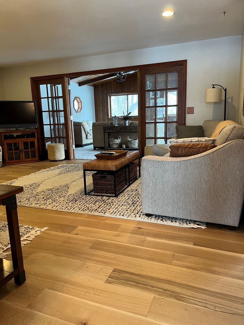 Cozy living room with gray sofa, glass coffee table, patterned rug, and wooden French doors to a bright room