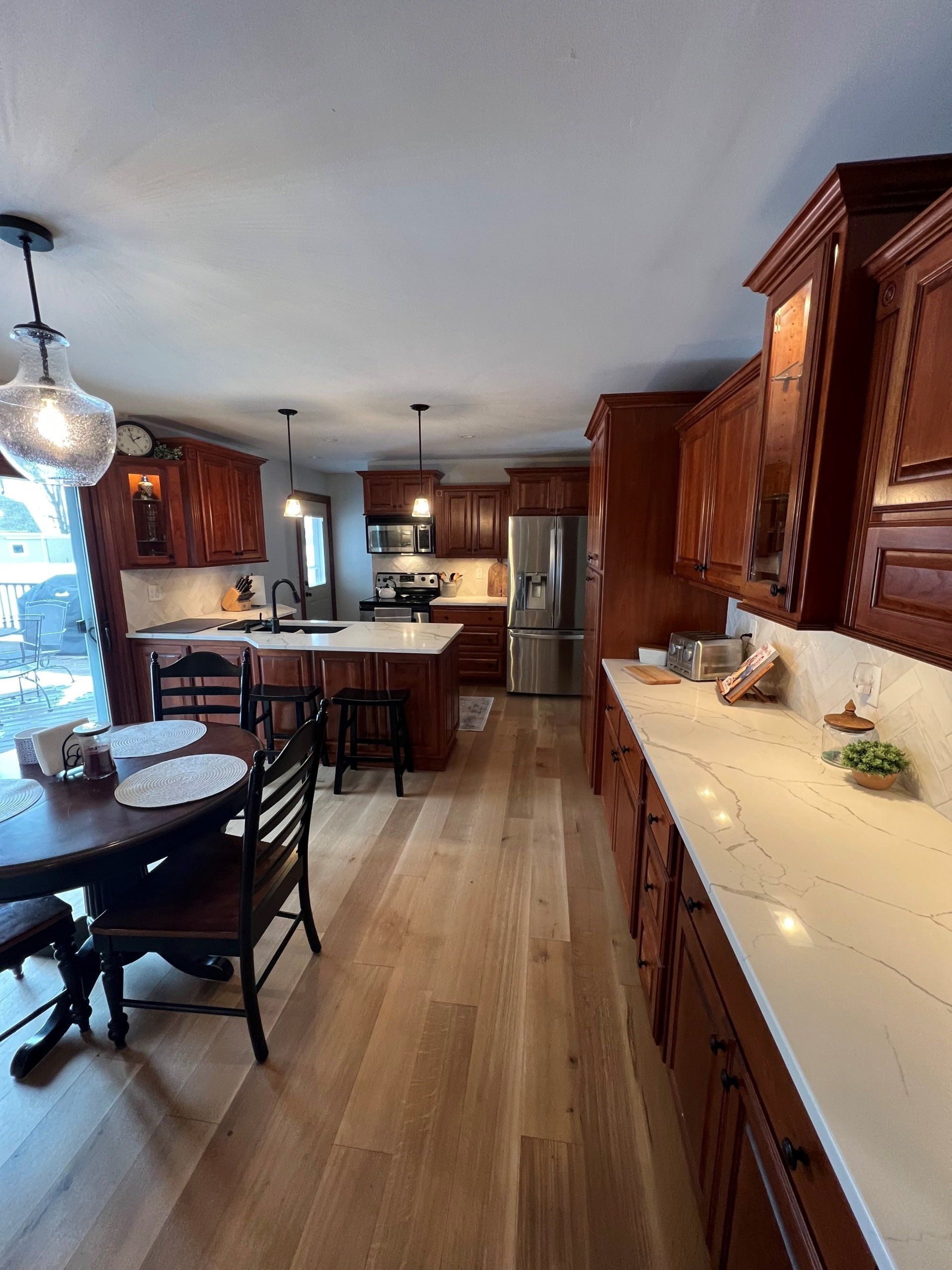 Warm wood kitchen with island, stainless steel fridge, long counter, and dining table by a window.