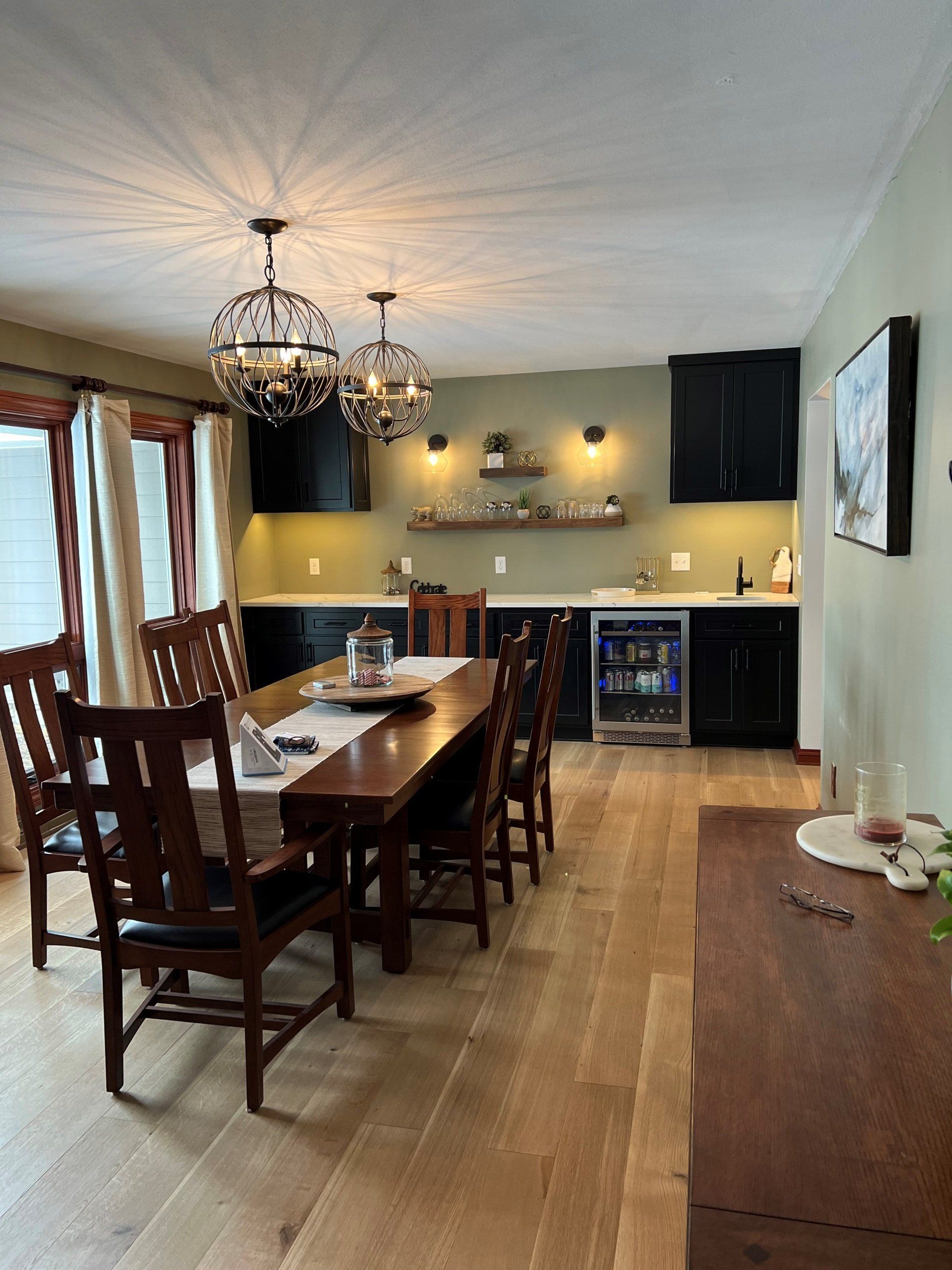 Dining room and kitchen with wood table, chandelier, dark cabinets, and light hardwood floors.