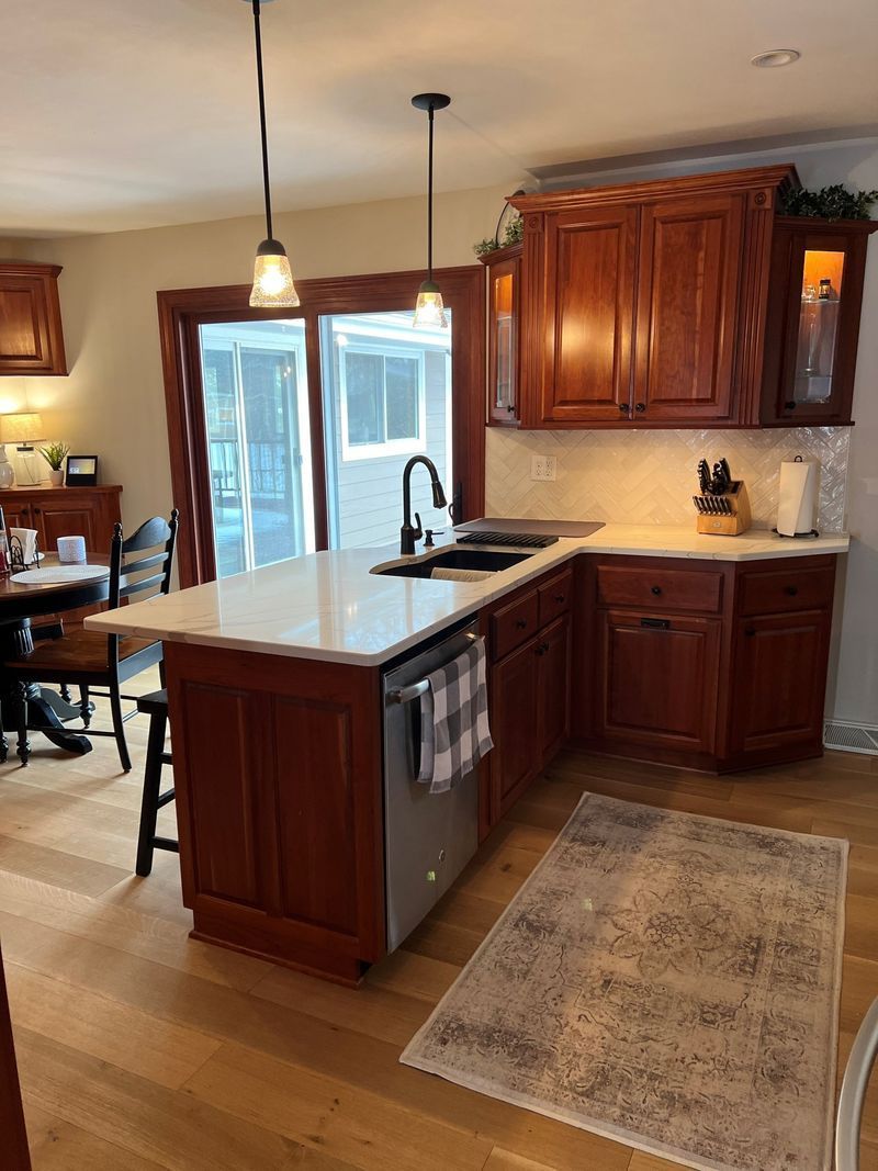 Modern kitchen with wooden cabinets, white island countertop, pendant lights, and a rug by the sink.