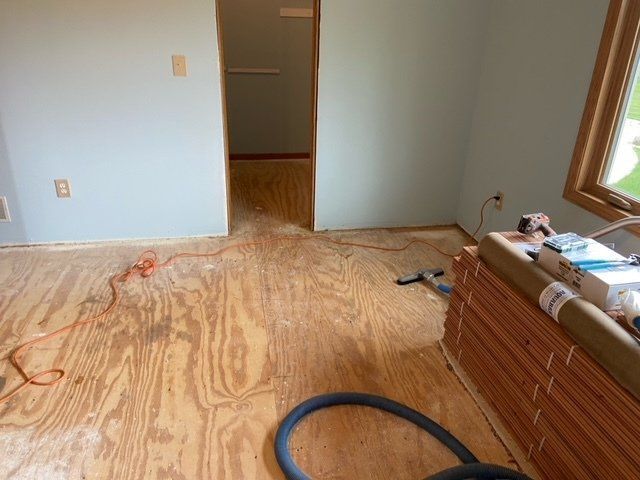 Unfinished room with bare plywood floor, open doorway, and tools/materials along the right wall.
