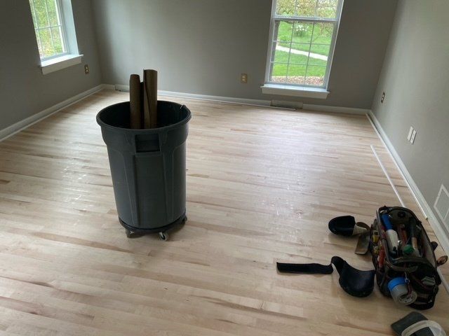 Empty room with hardwood floors, a trash can in the center, and a bag of tools on the right.
