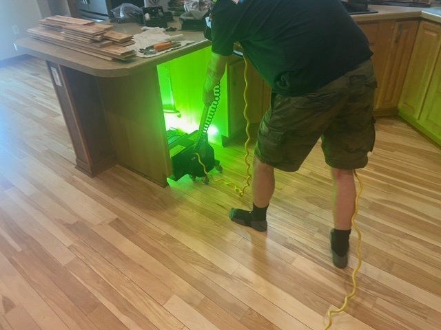 Person using a flashlight under a kitchen island with a bright green glow on the floor