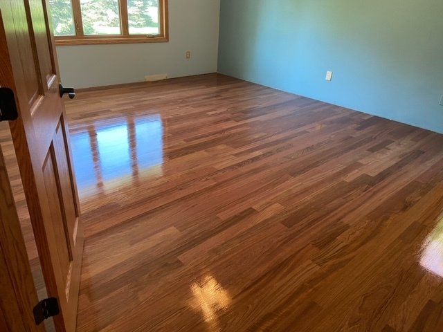 Empty room with shiny wood floors, blue accent wall, and a window letting in daylight.