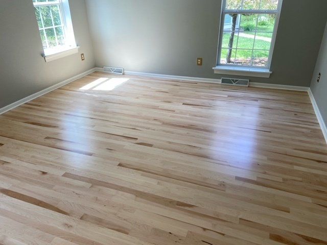 Empty room with light hardwood floors and two windows letting in sunlight