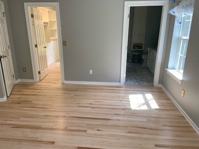 Empty room with light wood floor, gray walls, and open doorways to a hallway and adjoining rooms