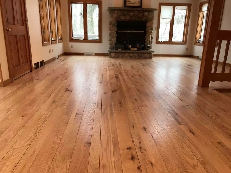 Empty wood-floored living room with large windows and a stone fireplace