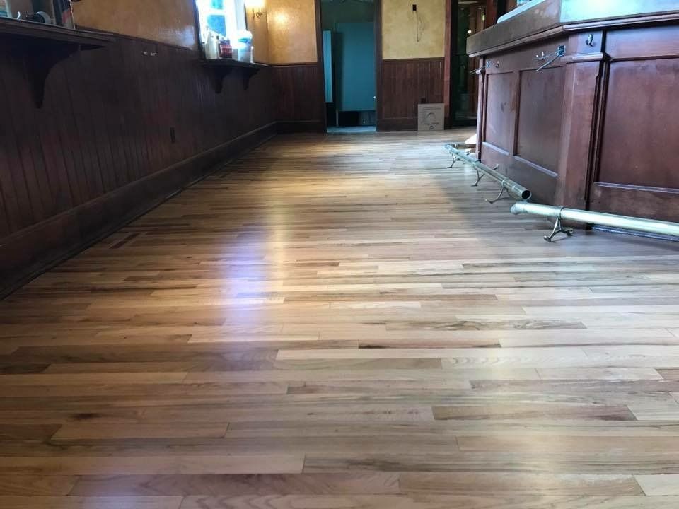 Empty wooden hallway with polished floor and paneled walls, lit by sunlight from a doorway ahead