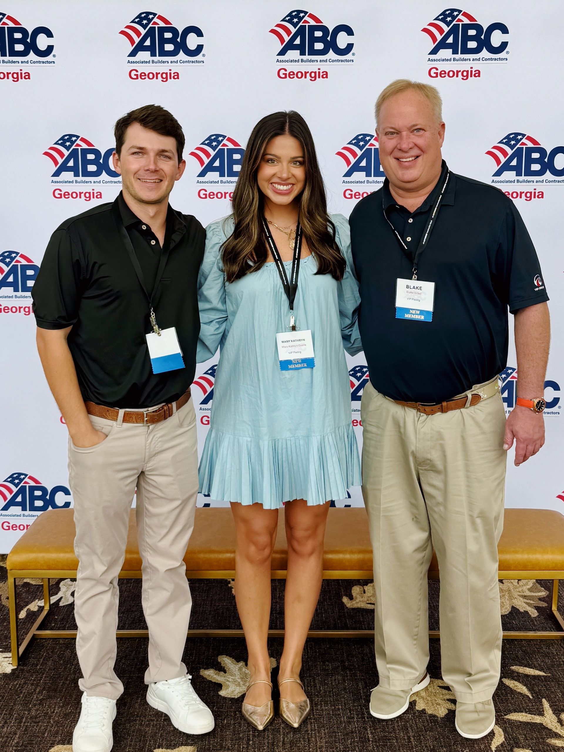 Three people posing in front of a backdrop with ABC Georgia logos. The woman in the center is wearing a blue dress.