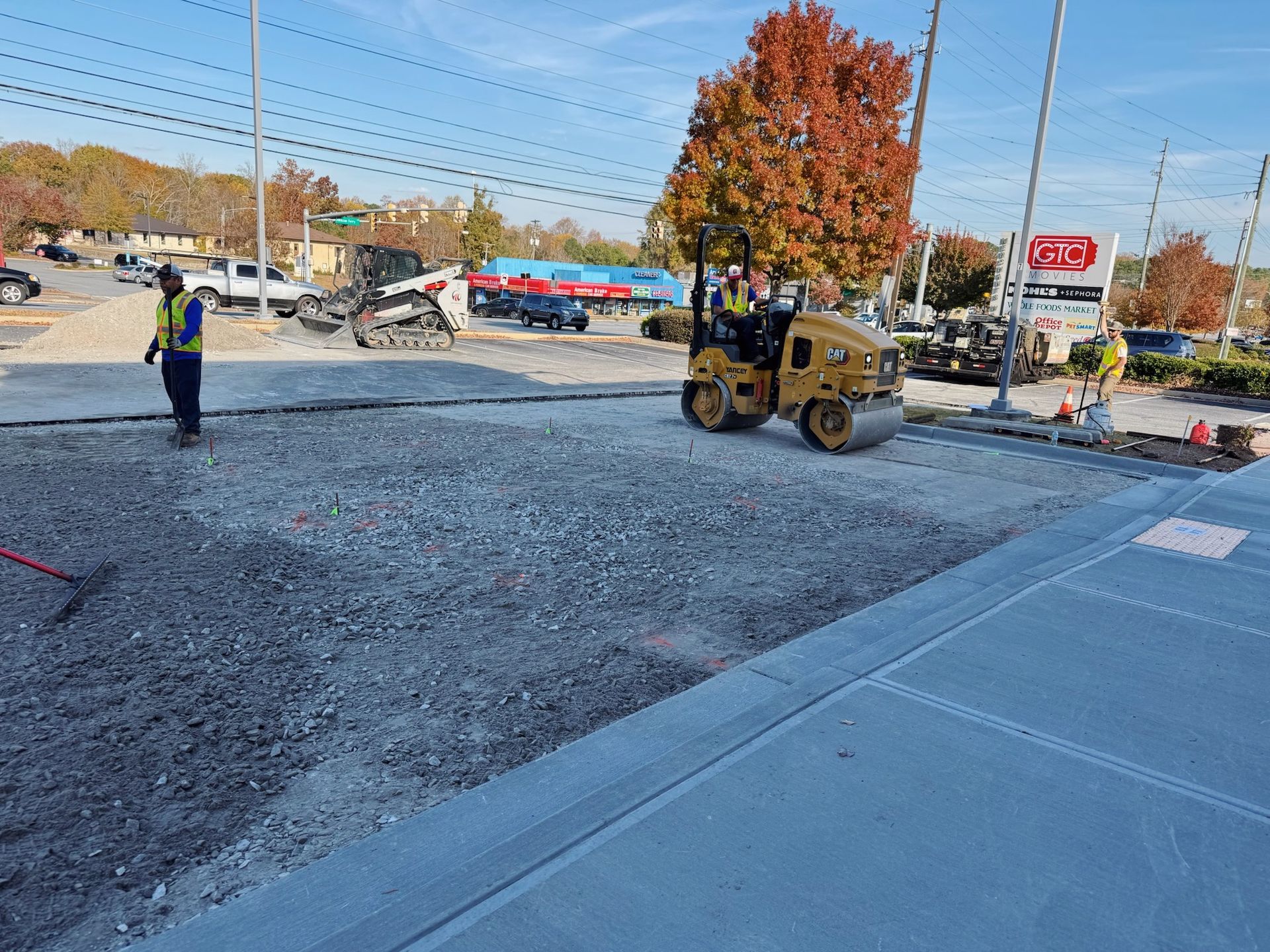 Construction site with a roller compacting gravel; workers observing.