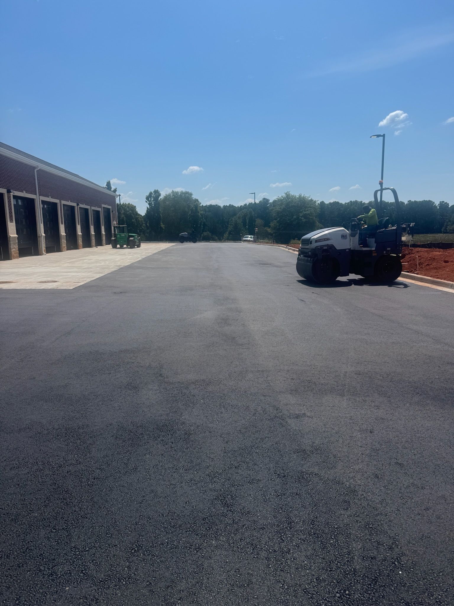 Newly paved asphalt road with a road roller under a blue sky.
