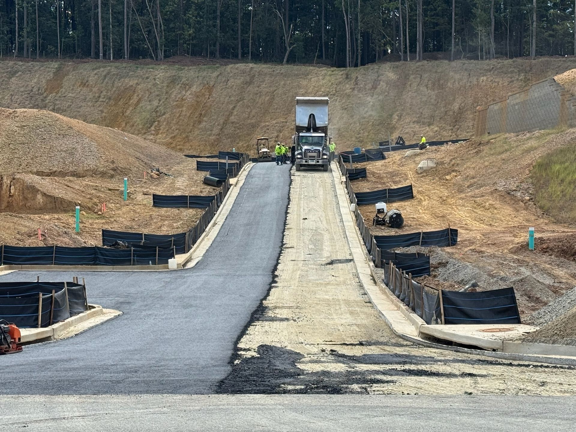 Construction site with truck on a paved ramp, surrounded by dirt walls and black barriers.