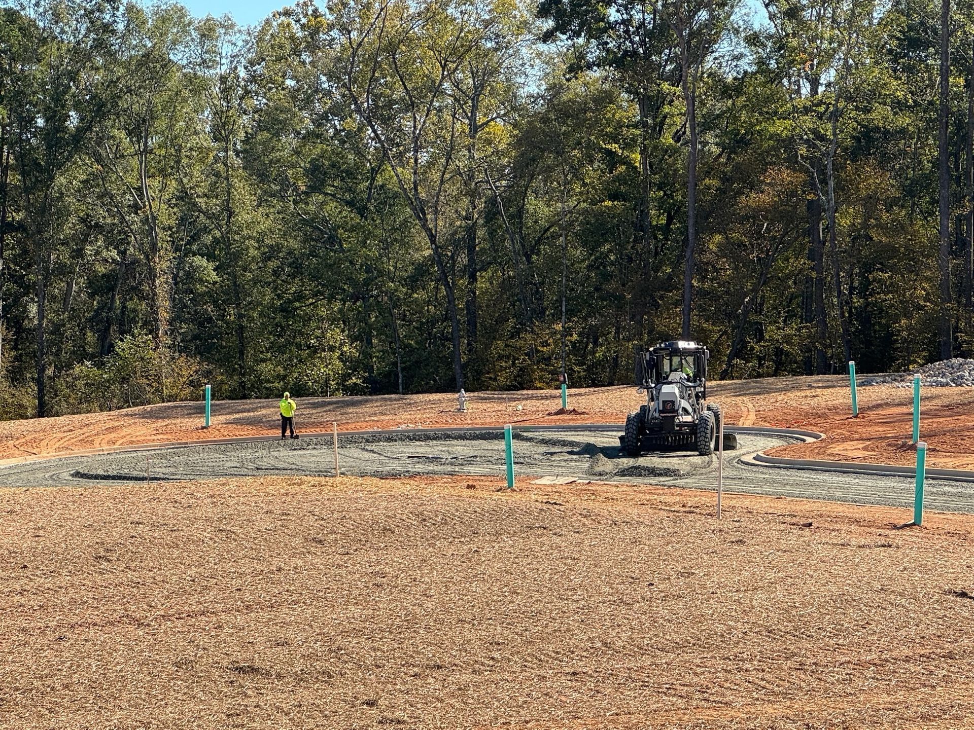 Construction site with a utility vehicle and worker in a high-visibility vest. Blue stakes mark the perimeter.