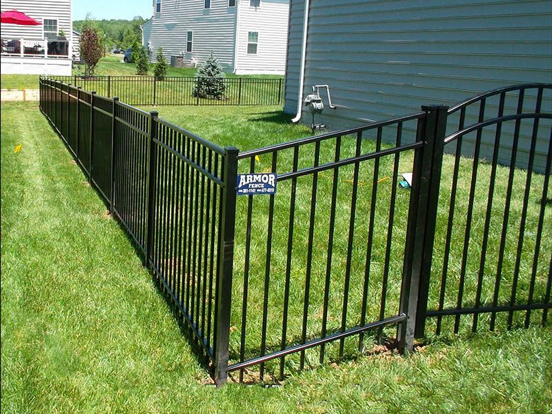 Black ornamental metal fence with a gate in a grassy backyard, bordering a house.
