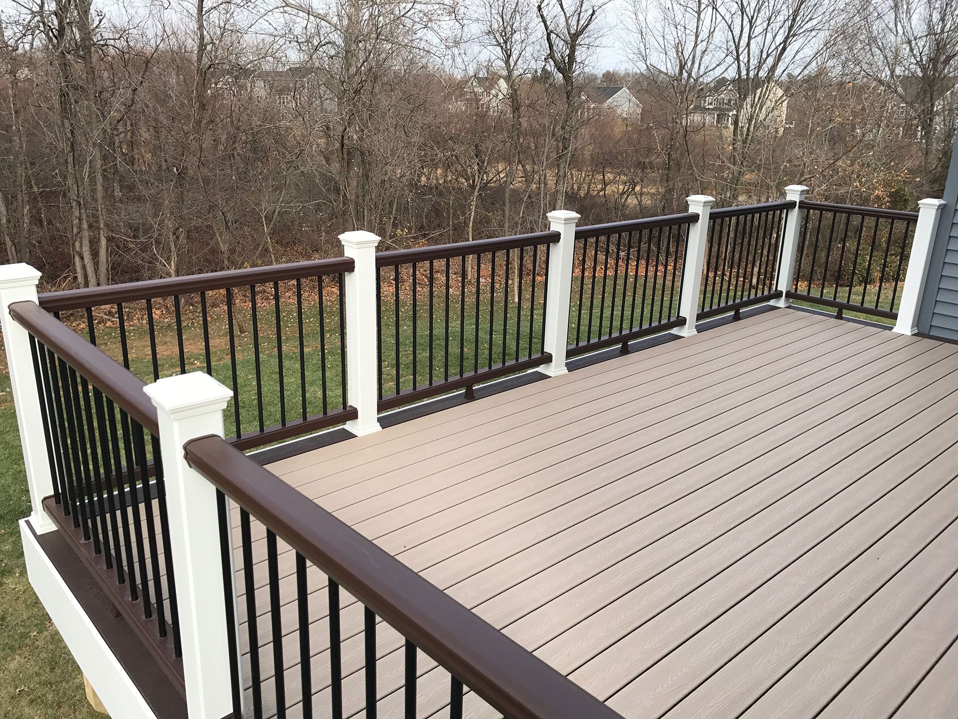 A well-built trex deck with brown and black railings and white posts overlooking a grassy backyard.