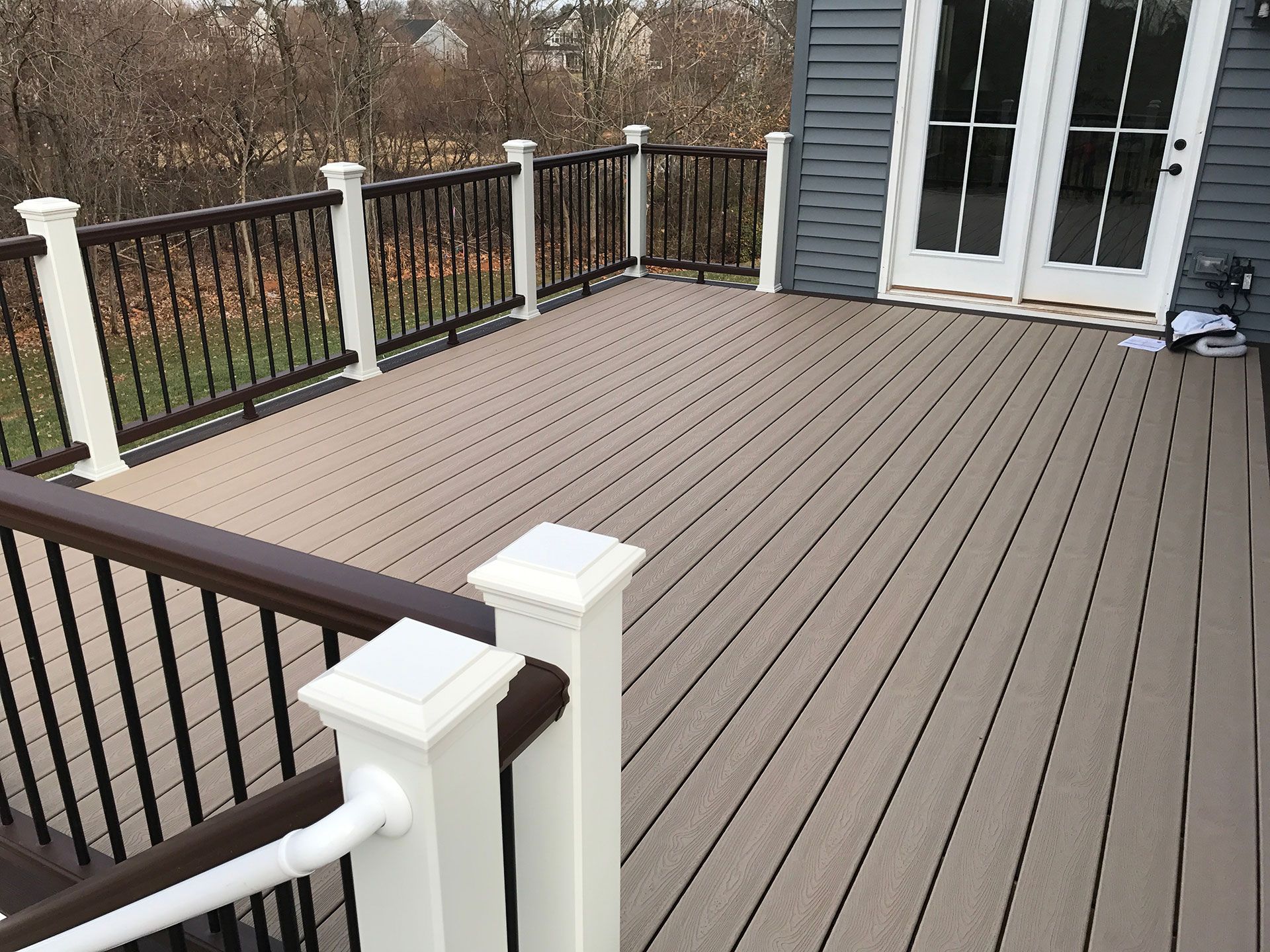 Trex deck with white posts, brown railings, and a brown composite deck surface. French doors are visible on the right.