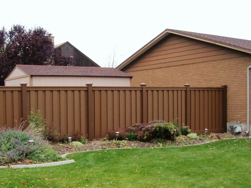 Trex fencing in a backyard with a shed and house visible, green grass and landscaping in front.