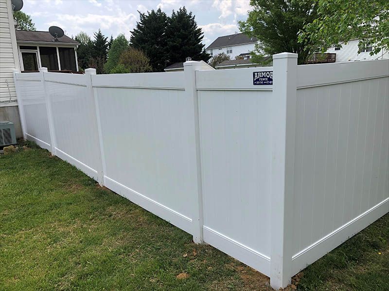 White vinyl privacy fence in a backyard, with grass and trees in the background.