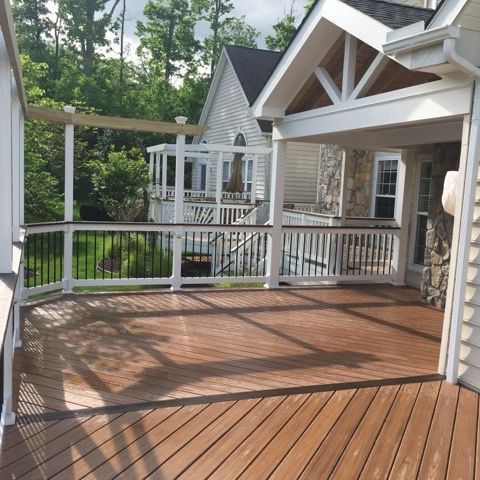 A wooden deck with a white railing and pergola, overlooking a backyard. The deck is brown, and a house is visible in the background.