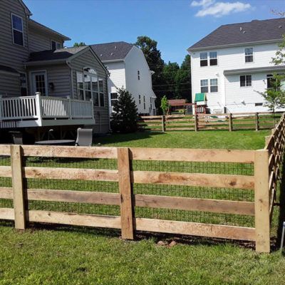 Wooden fence in a grassy backyard, with houses in the background under a blue sky.