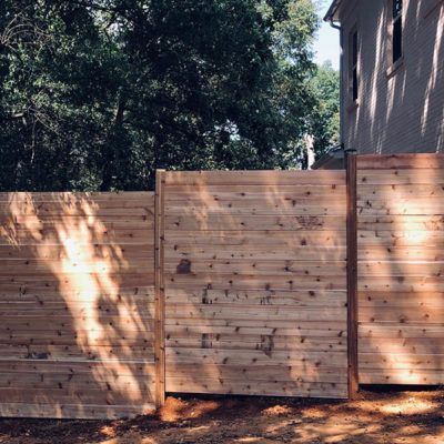 A wooden fence is sitting in front of a house with trees in the background.