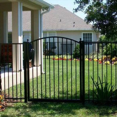 A black metal fence surrounds a lush green yard in front of a house.