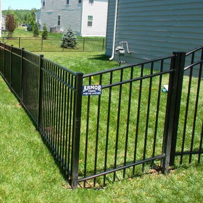 A black metal fence surrounds a lush green yard in front of a house.