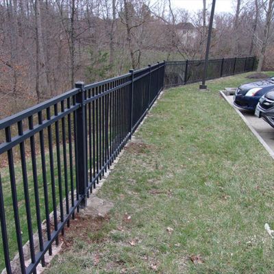 A black fence surrounds a parking lot with cars parked behind it.