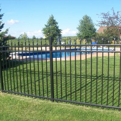 A black metal fence surrounds a swimming pool in a backyard.