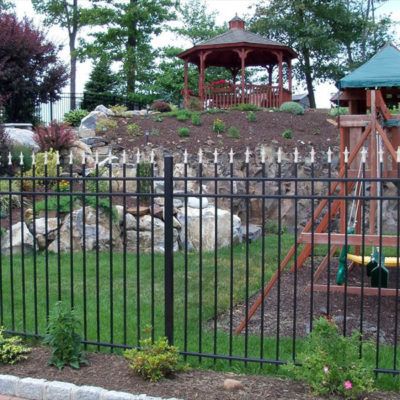 A black fence surrounds a playground with a gazebo in the background