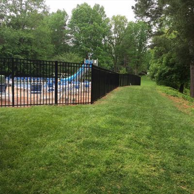 A black fence surrounds a swimming pool and a playground.
