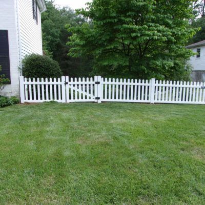 A white picket fence surrounds a lush green lawn in front of a house.