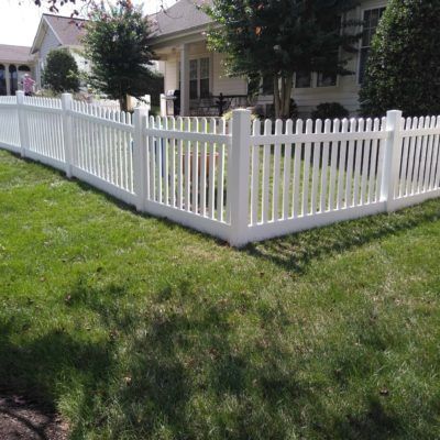 A white picket fence surrounds a lush green yard in front of a house.