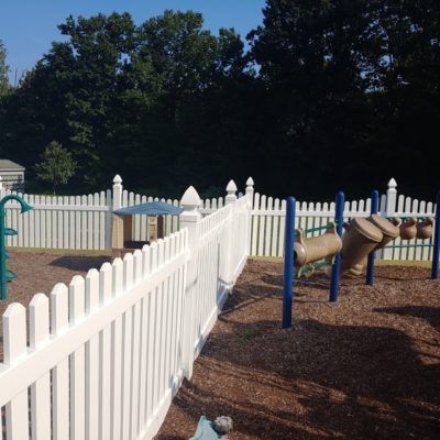 A playground with a white picket fence surrounding it