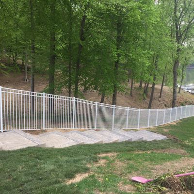 A white fence surrounds a grassy area with trees in the background.