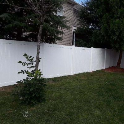 A white vinyl fence surrounds a lush green yard.