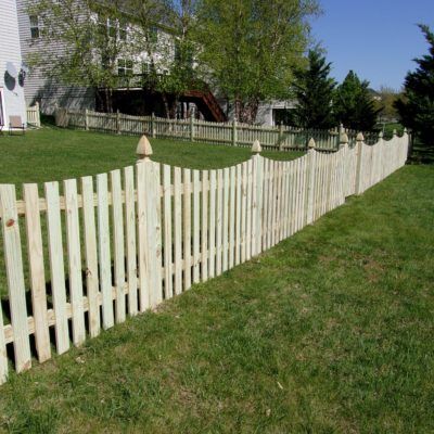 A wooden picket fence is sitting in the middle of a lush green field.