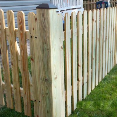 A wooden picket fence is sitting in the grass in front of a house.