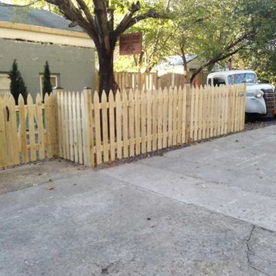 A white truck is parked behind a wooden picket fence
