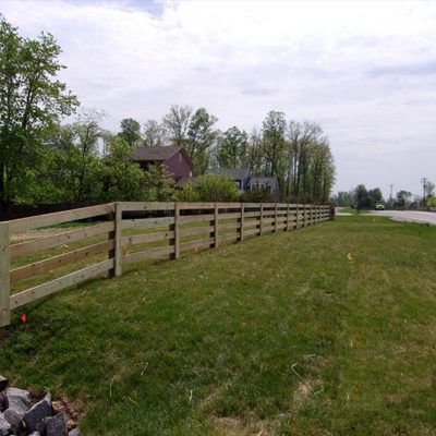 A wooden fence surrounds a grassy field next to a road.
