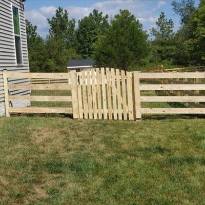 A wooden fence with a gate in the middle of a lush green field.