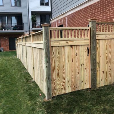 A wooden fence with a gate in front of a brick building.