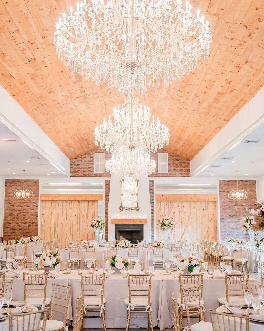 Elegant wedding reception hall with chandeliers, tables set for guests, and a wooden ceiling.