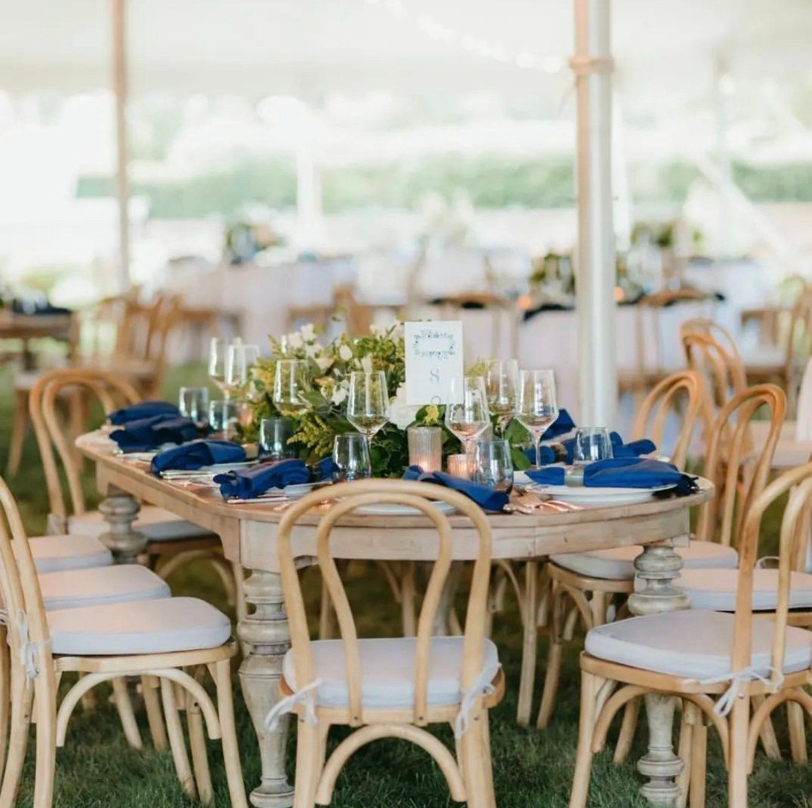 Wedding reception table set with blue napkins and white flowers, under a tent.