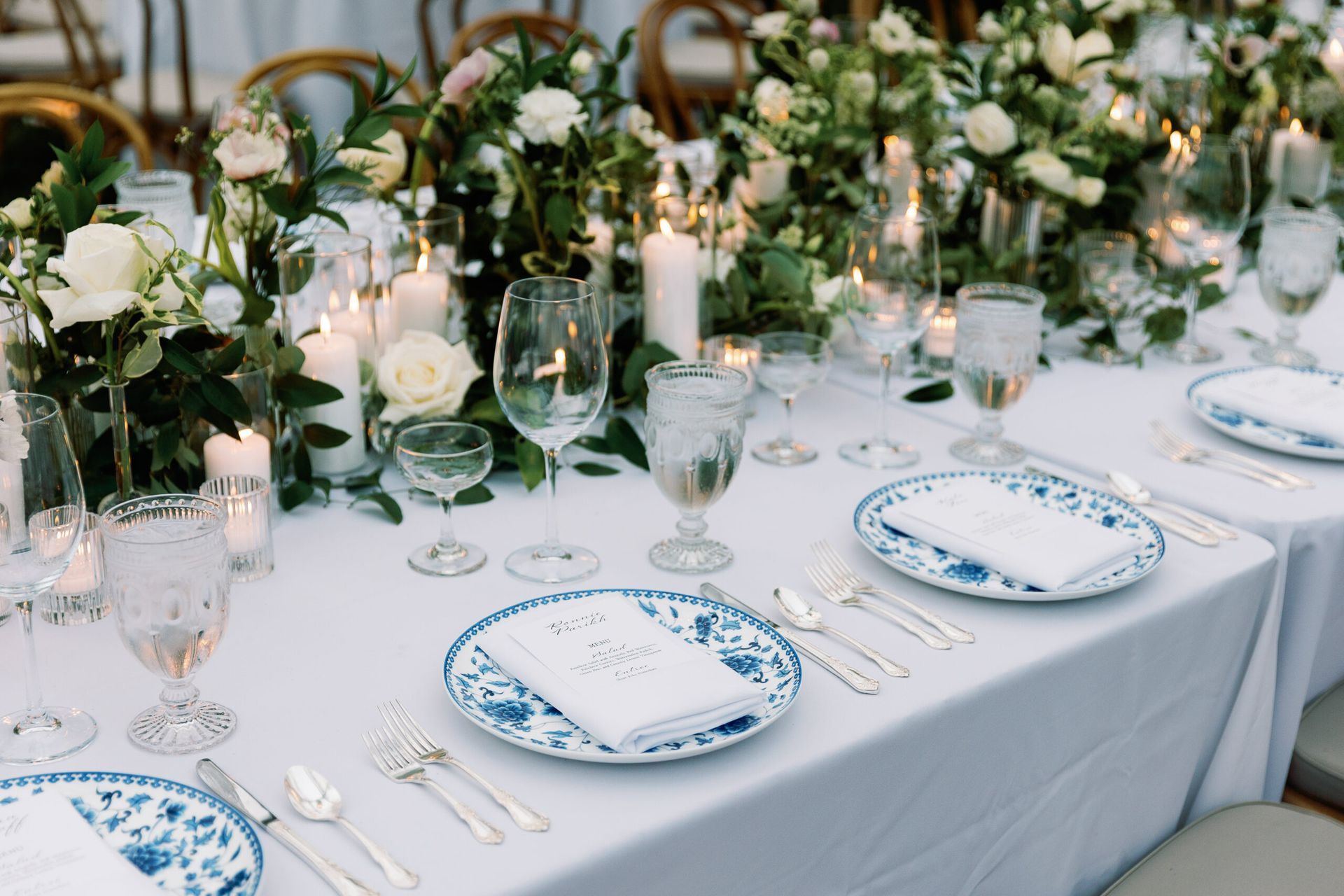 Formal table setting with blue and white patterned plates, crystal glasses, and white flowers and candles as a centerpiece.