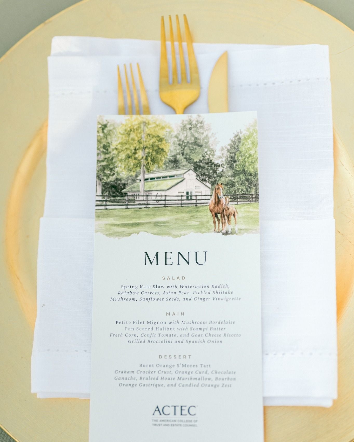 A place setting with a white napkin, gold flatware, and a menu card featuring a horse and barn scene.